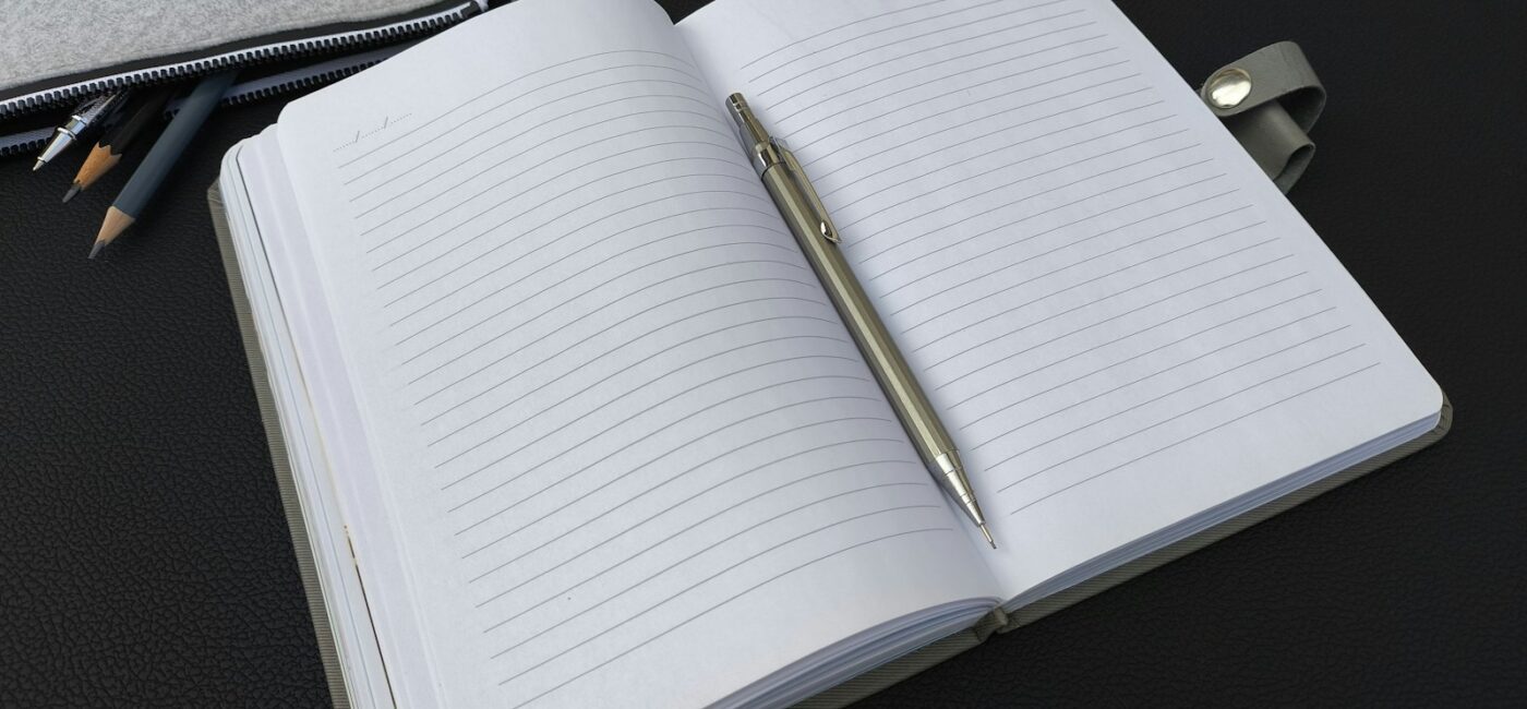 SMART-Ziele formulieren: Persönliche Ziele klären und konkret planen Ein Stift liegt in einem aufgeschlagenen linierten Notizbuch, daneben ein Mäppchen mit Stiften.
