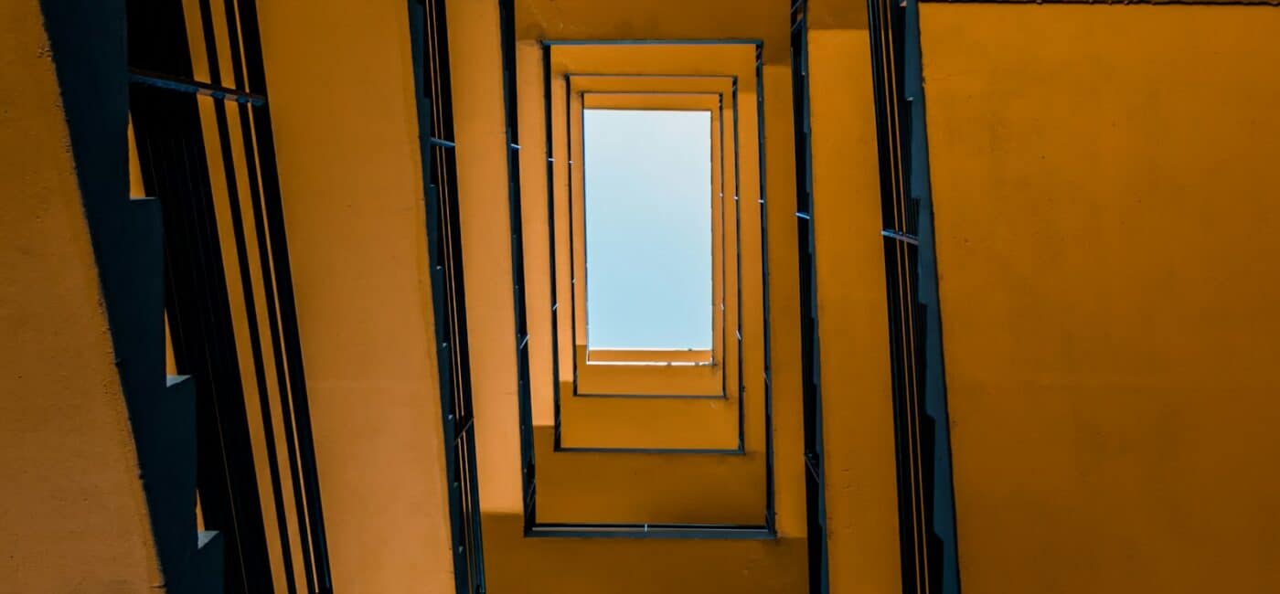 Blick von unten durch ein gelbes Treppenhaus zum blauen Himmel.