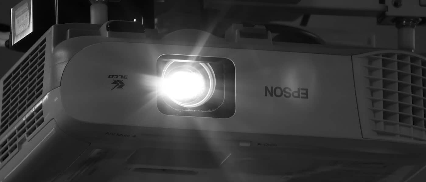 Ein eingeschalteter Projektor wirft einen hellen Lichtstrahl in einen dunklen Raum.